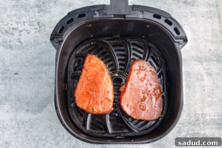 Two ahi tuna steaks cooking in an air fryer basket, showing a perfect sear.