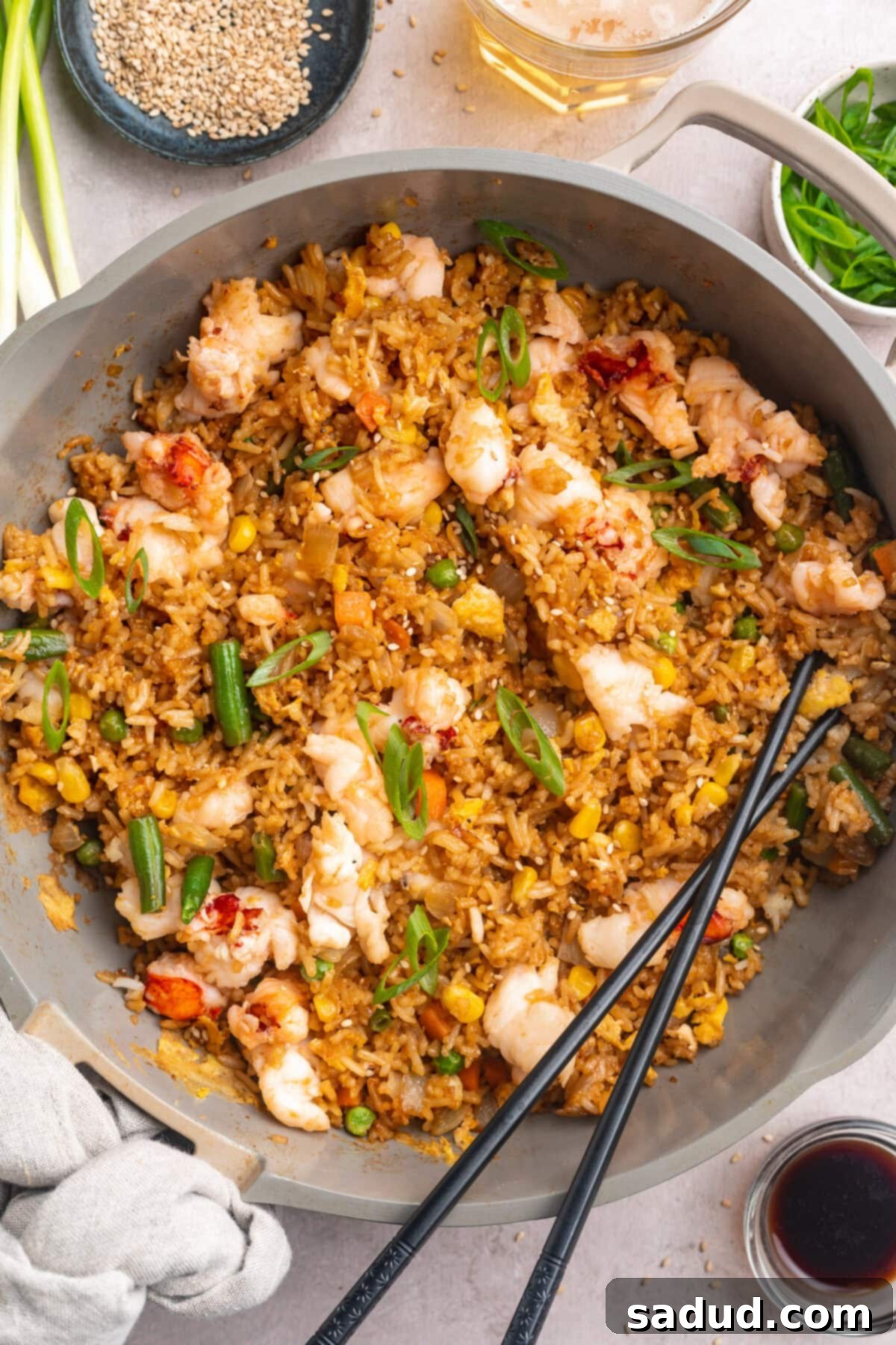 A large grey shallow bowl holding lobster fried rice with veggies and a set of black chopsticks resting on the edge of the bowl. 