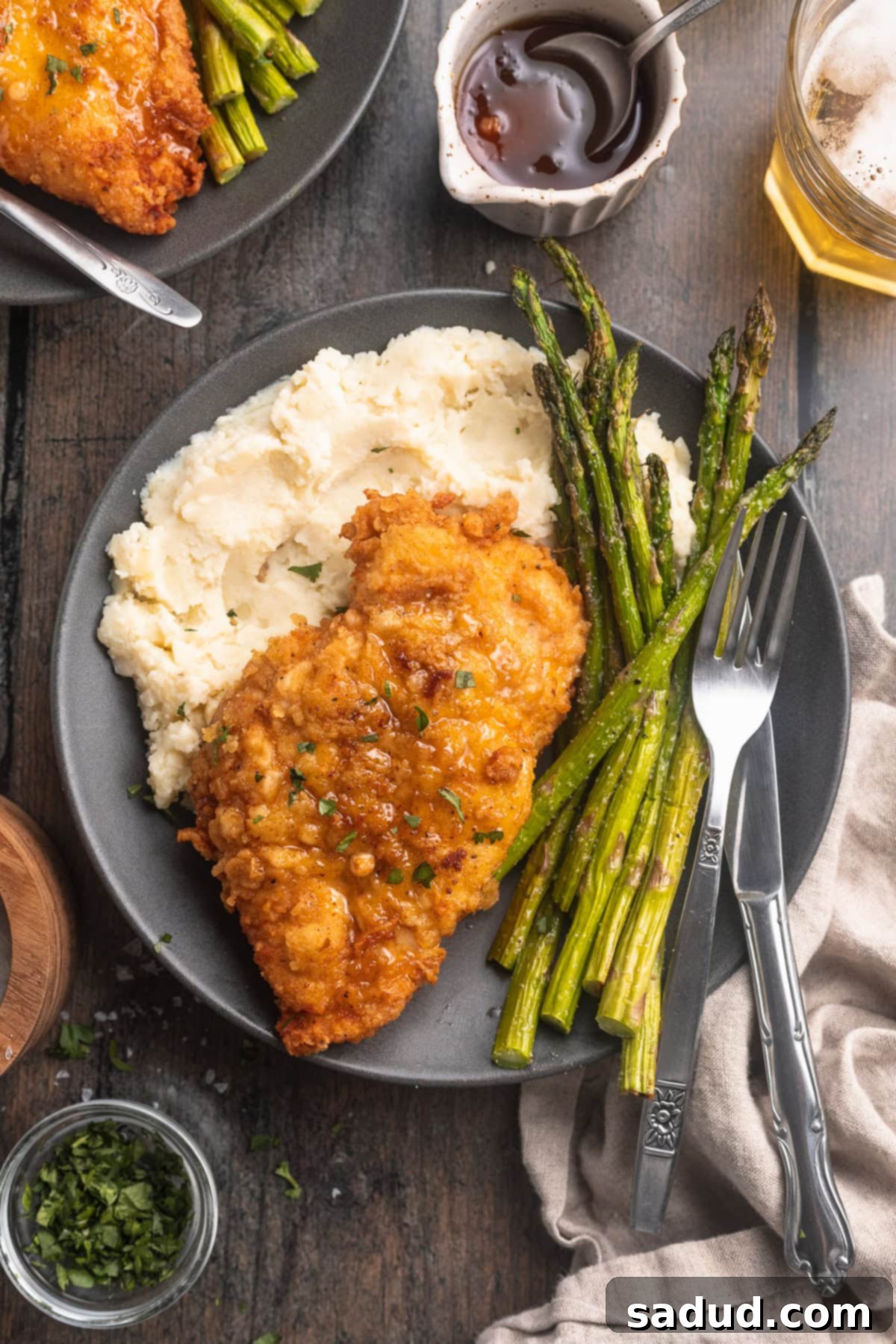 Truffle honey chicken plated with crisp, bright green asparagus and a bed of fluffy mashed potatoes, highlighting the rich flavors and textures.