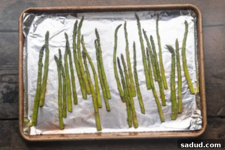 Asparagus spears evenly spread on a baking sheet lined with aluminum foil, ready for roasting.