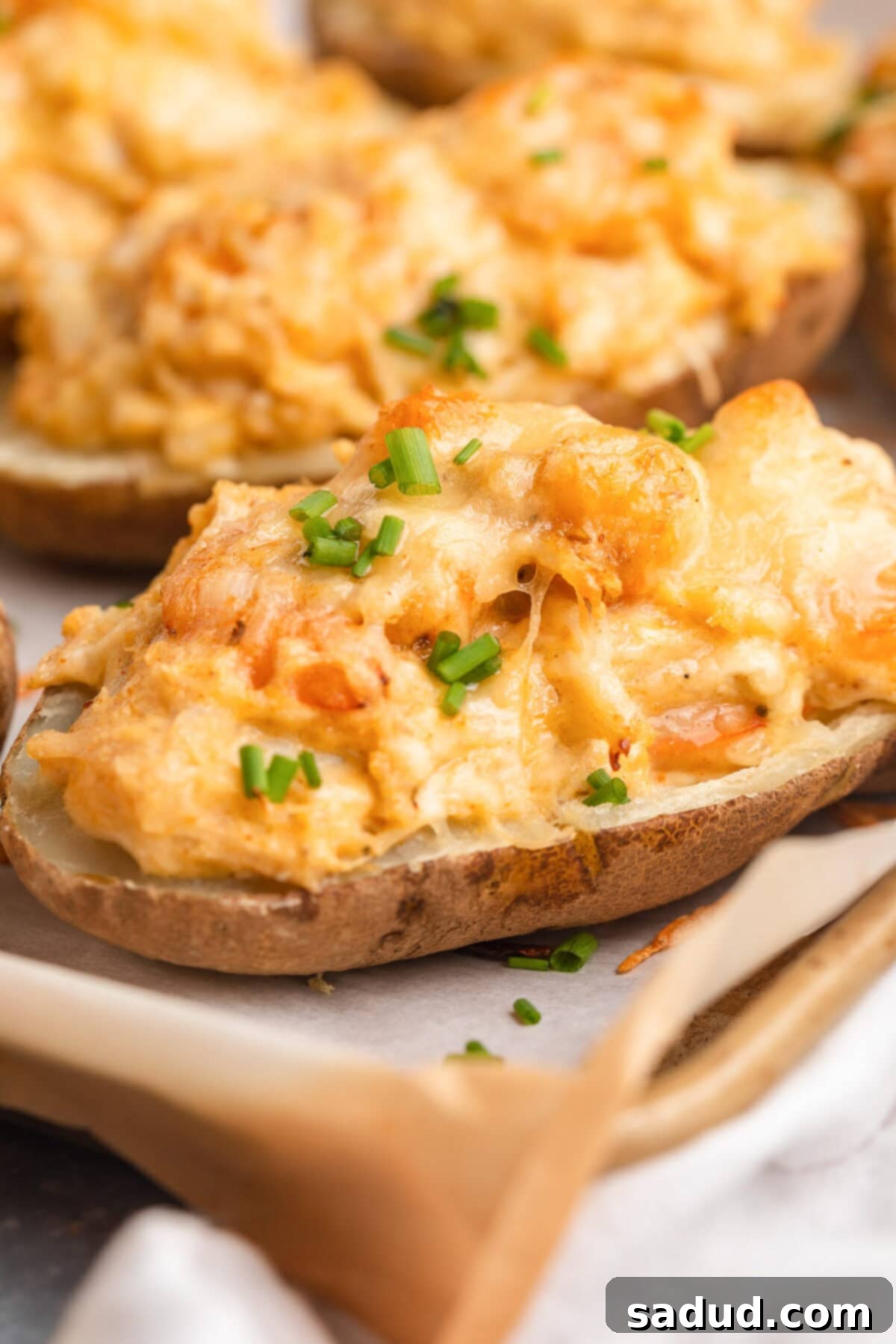 Seafood-stuffed baked potatoes resting on a baking sheet lined with tan parchment paper, showcasing golden melted cheese and a vibrant filling.