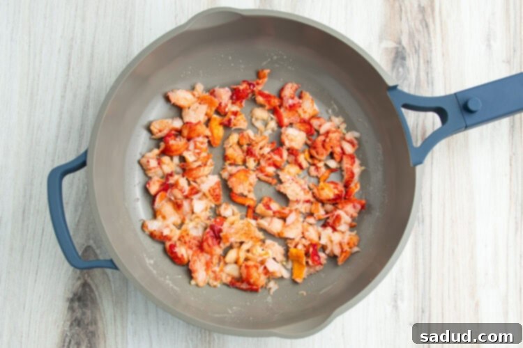 Cooked lobster meat being warmed in a large skillet with butter and garlic.
