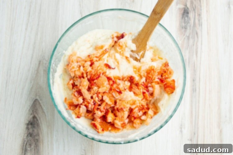 Warm lobster and mashed potatoes being combined in a large glass mixing bowl.