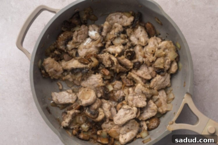 Strips of pork tenderloin in large skillet with sautéed mushrooms and diced onions.