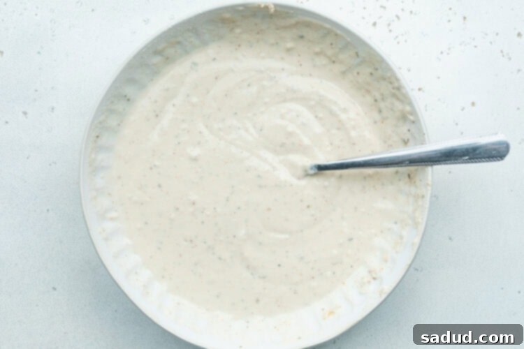 Batter mixture for vegan chicken fillet breading in a large white bowl with a spoon.