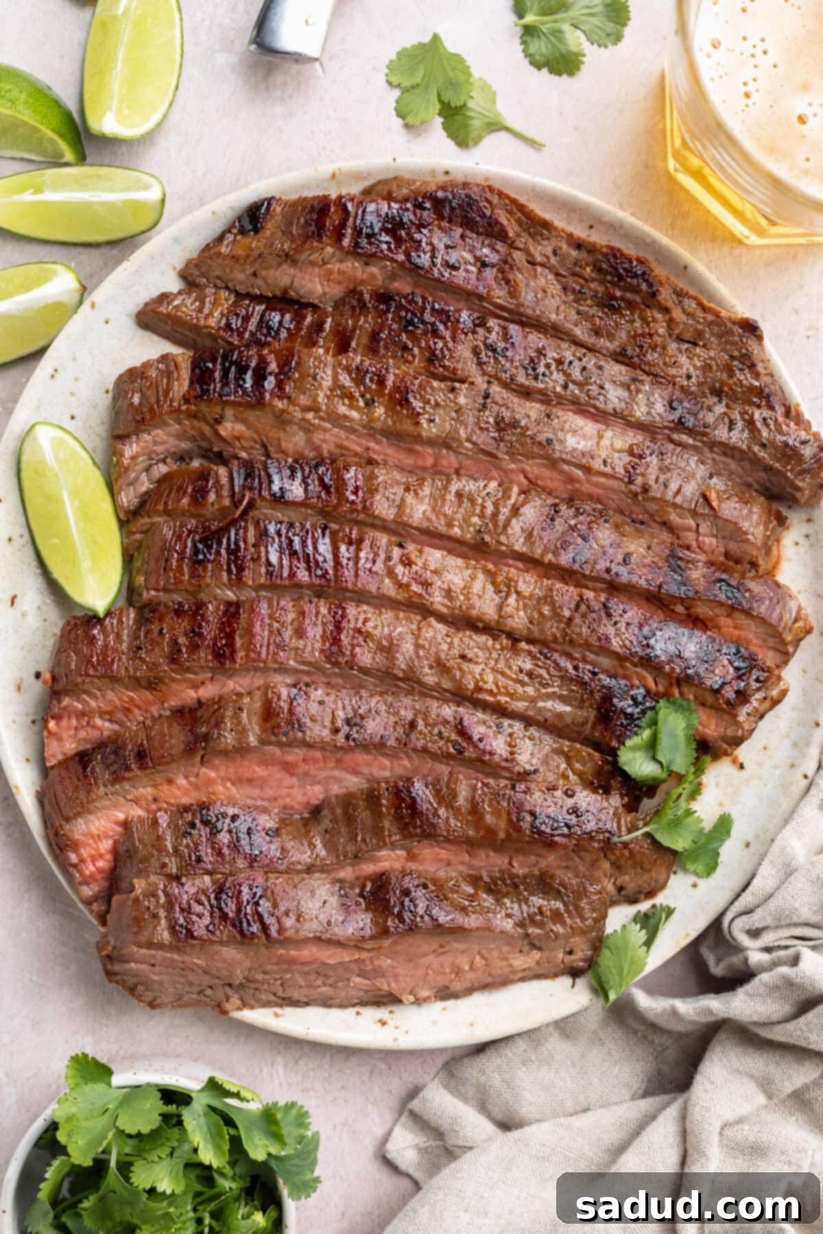 Top-down view of a sliced, sous-vide cooked flank steak on a white plate surrounded by lime wedges and other garnish. This perfectly cooked flank steak showcases its tender interior.