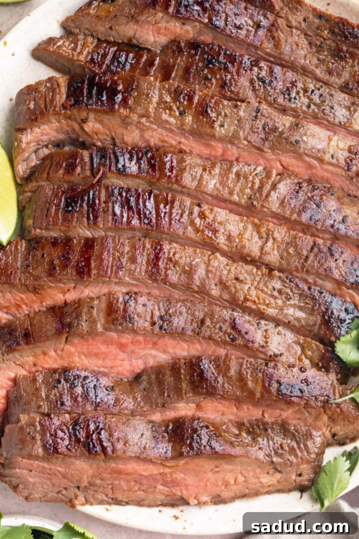Close-up view of thickly sliced sous vide flank steak on a white plate with lime wedges, showcasing its tender texture and perfectly cooked interior.