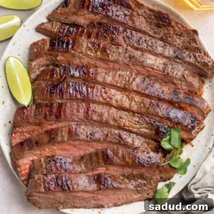 Top-down view of a sliced, sous-vide cooked flank steak on a white plate surrounded by lime wedges and other garnish. This image highlights the beautiful color and texture of the perfectly cooked flank steak.