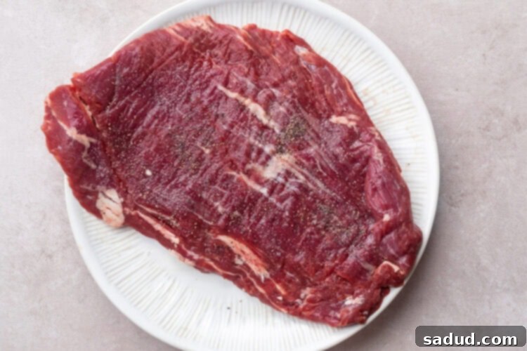 Seasoned flank steak on a round white plate, ready for marinating.
