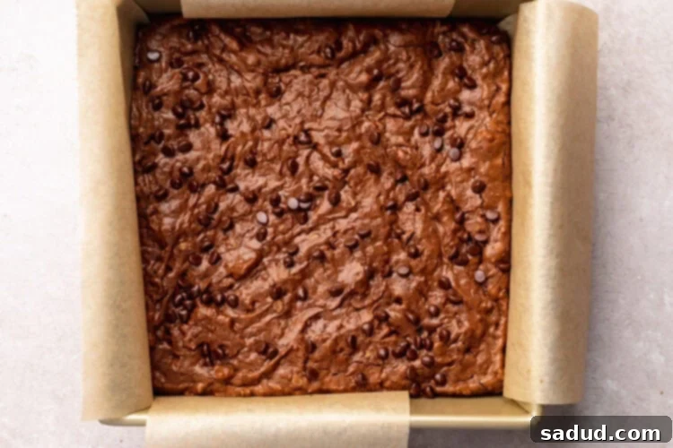 Top-down view of fully baked chocolate lactation brownies in a square baking pan with parchment paper hanging out the sides.