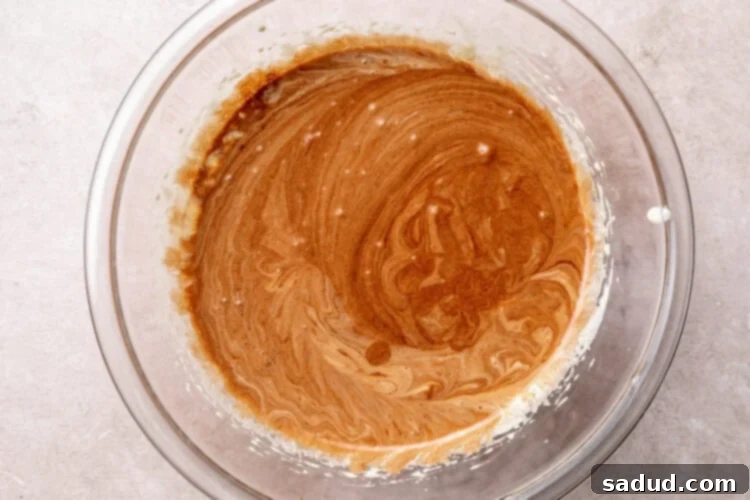 Melted chocolate added to sugar and egg mixture in large glass mixing bowl.