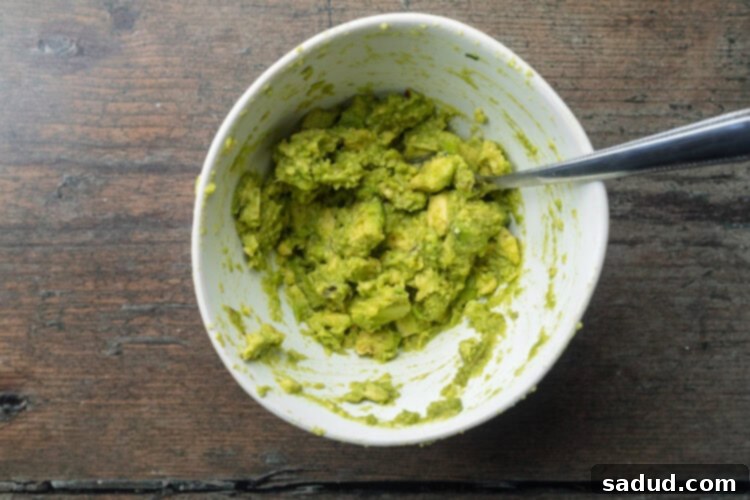 Mashed avocado with lime juice and salt in a mixing bowl with a fork.
