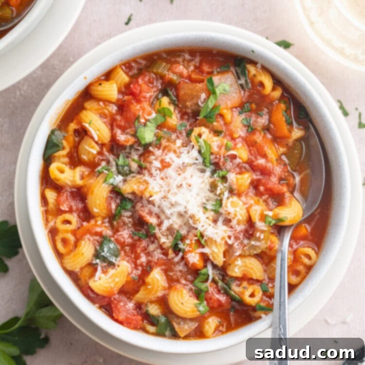 A white bowl of tomato florentine soup on a white tabletop, garnished with fresh basil leaves.