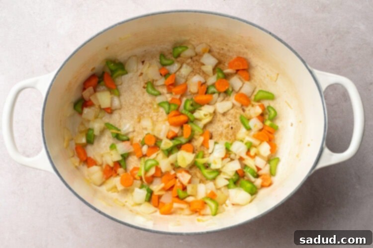 Top-down view of a large stock pot with oil, onions, carrots, and celery sautéing.