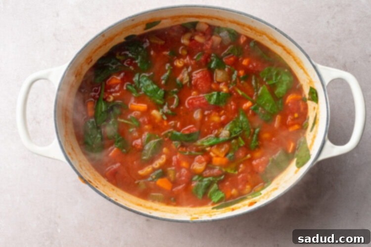 Top-down view of tomato florentine soup with wilted spinach in a large oval stockpot.