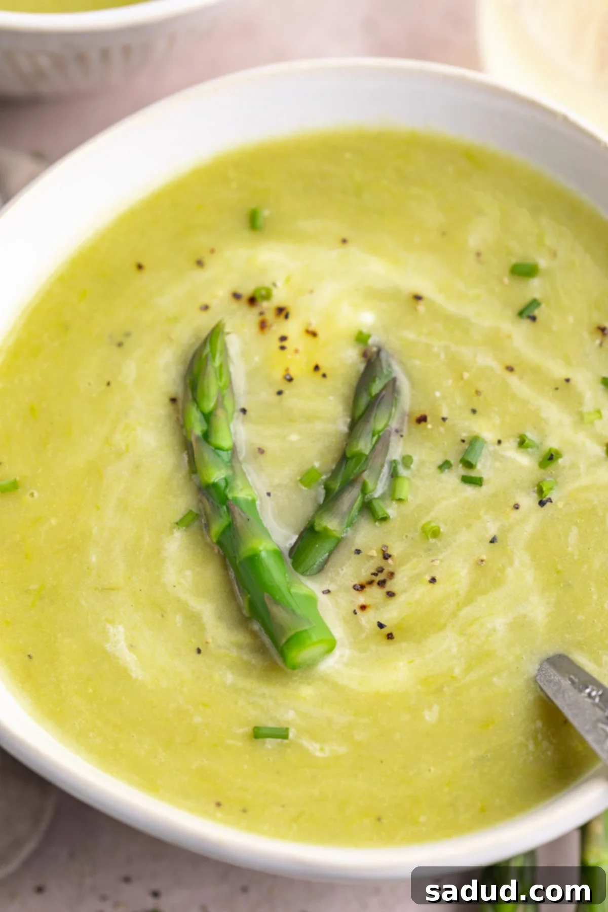Close-up, angled view of a white bowl of potato asparagus soup garnished with asparagus.