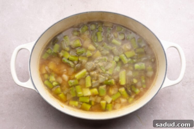 Asparagus, broth, and other ingredients for potato asparagus soup in a large dutch oven.
