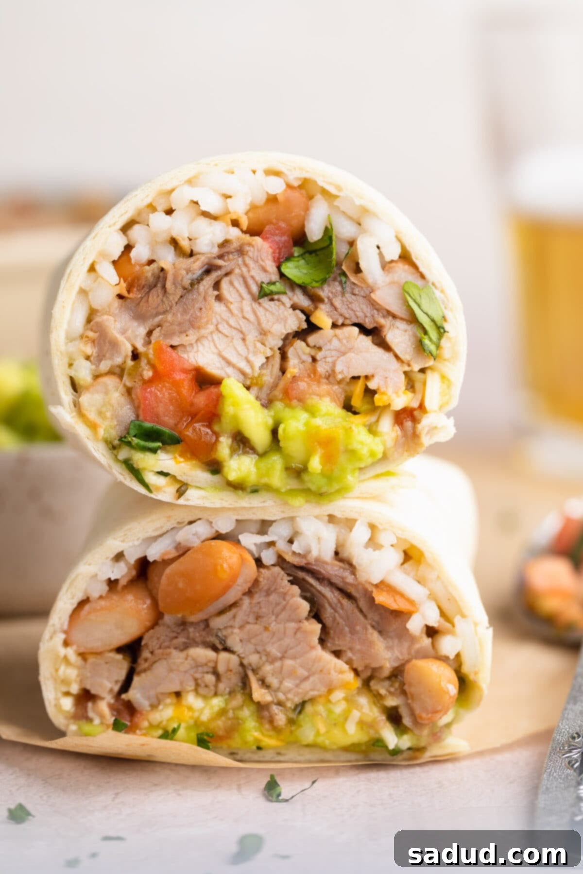 The Ultimate Carnitas Experience 2 Cross section of a carnitas burrito, with the two halves stacked on top of each other to show ingredients inside.