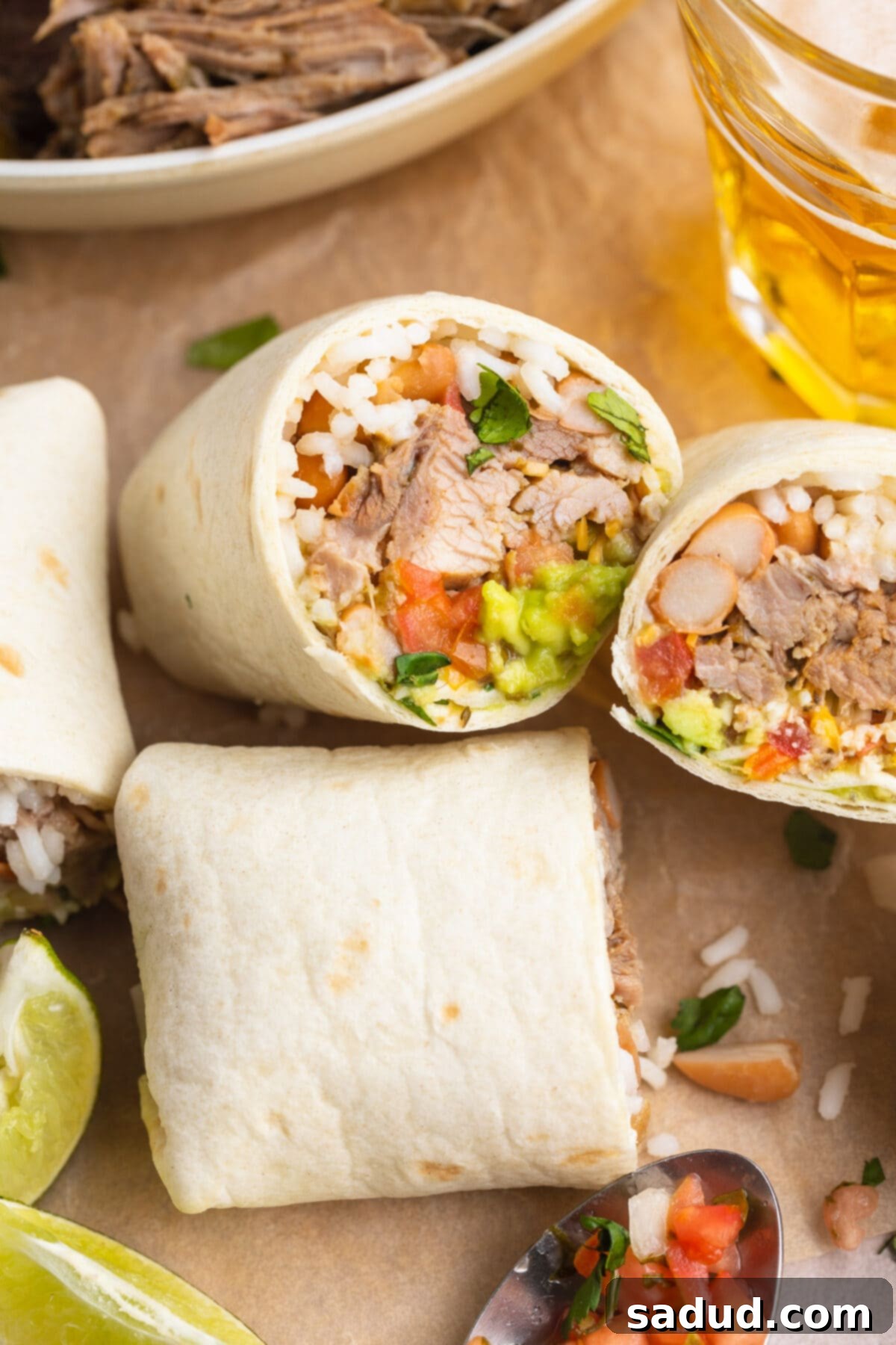 The Ultimate Carnitas Experience 3 Two carnitas burritos cut in half and laying on a sheet of parchment paper.