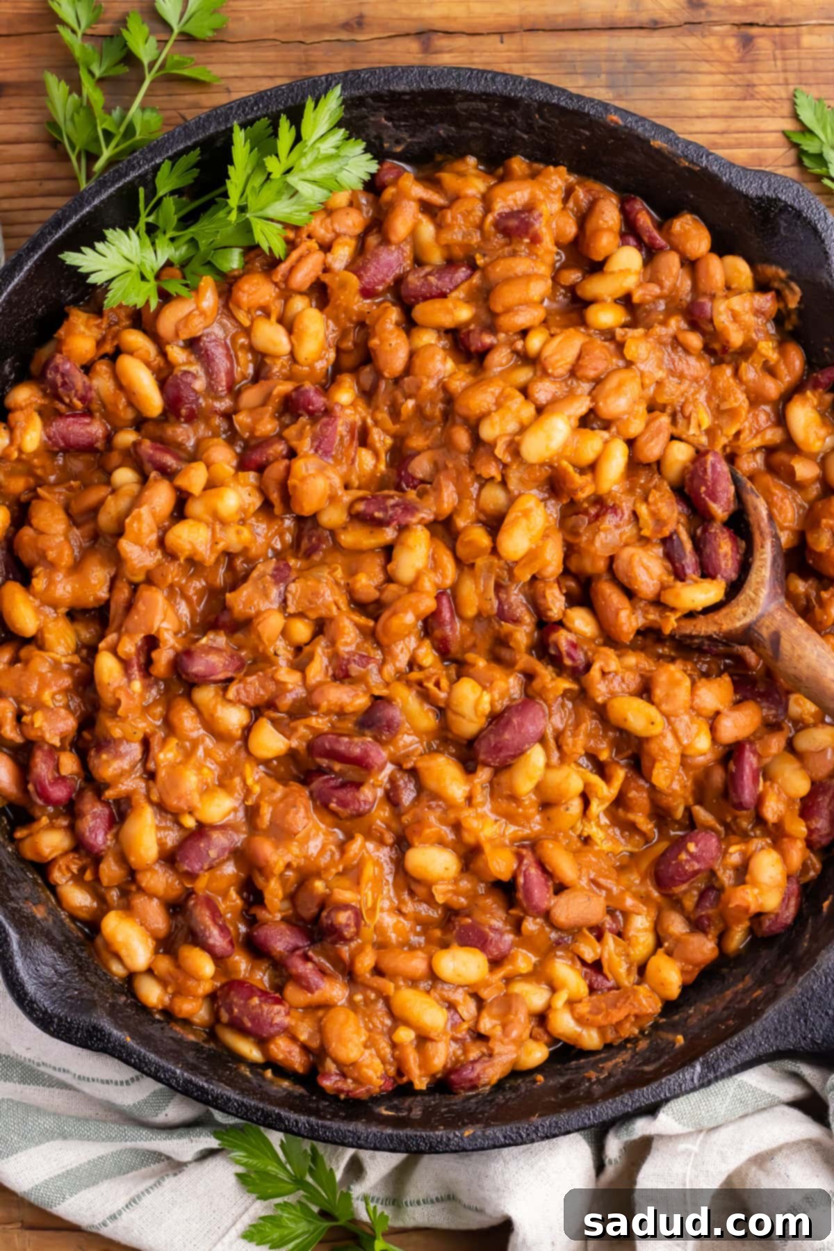 Overhead view of a cast-iron skillet filled with perfectly cooked smoked baked beans, ready to serve with a wooden spoon.