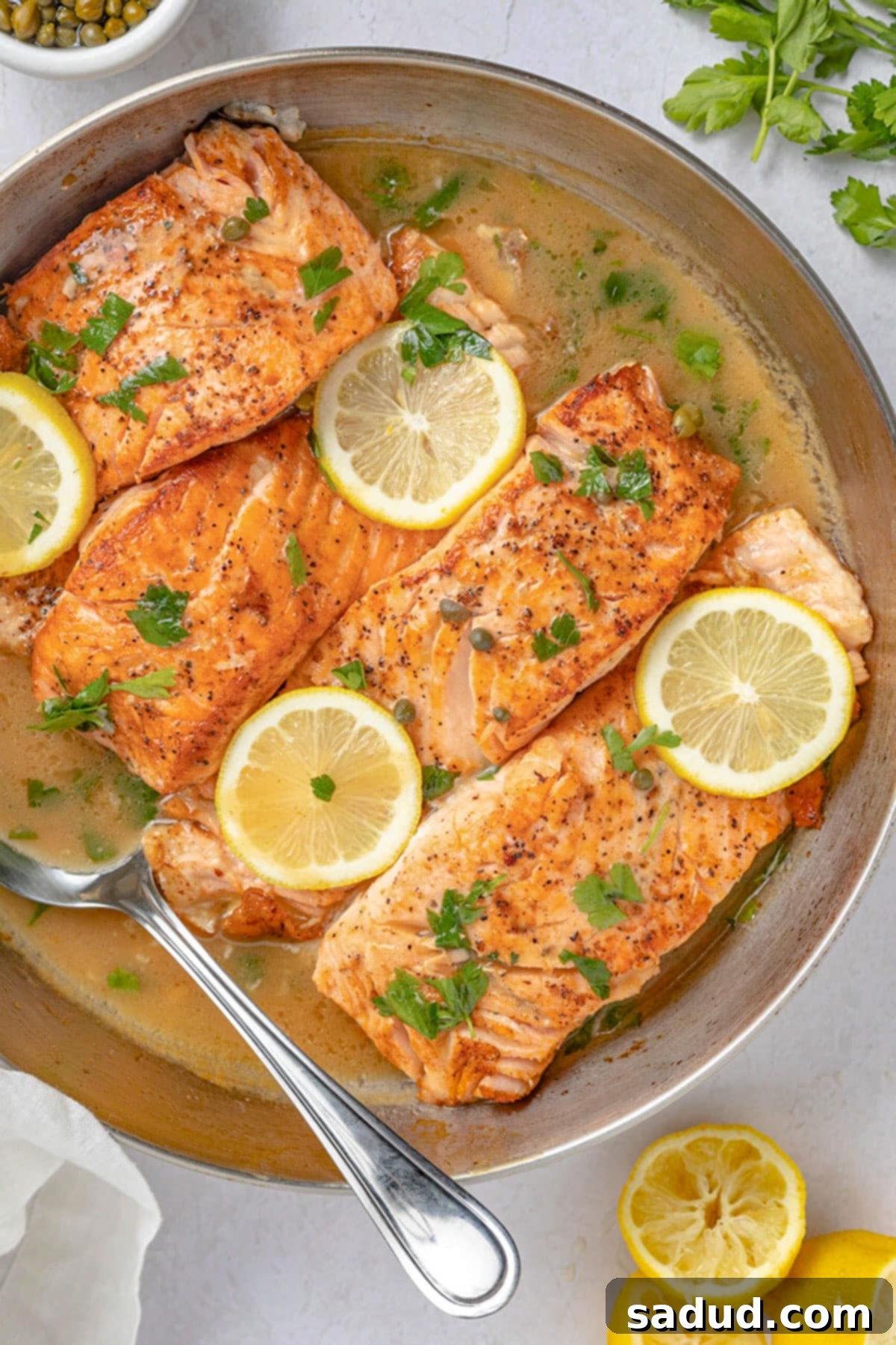 4 salmon fillets in a large silver saucepan with lemon discs and a butter sauce.