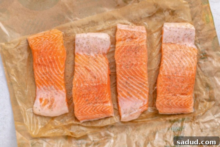 Salmon slices on parchment paper with salt and pepper.