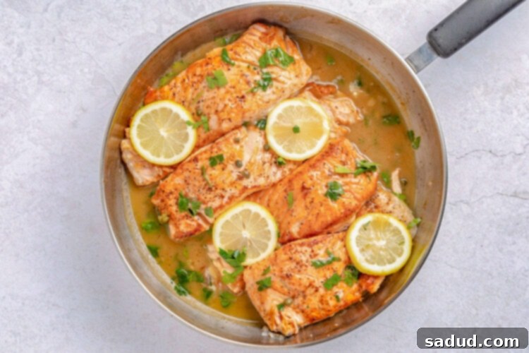 Salmon piccata in a large silver skillet with lemon coins and parsley to garnish.