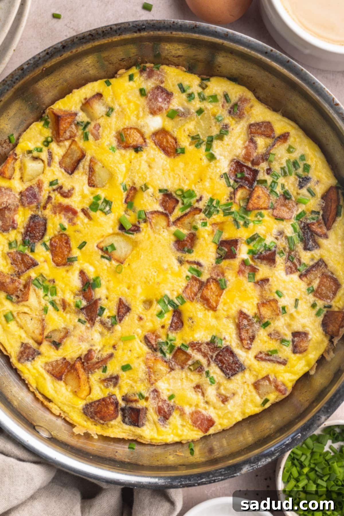 A large country omelette in a large silver skillet, ready to be served, showcasing the golden-brown potatoes and crispy bacon bits.