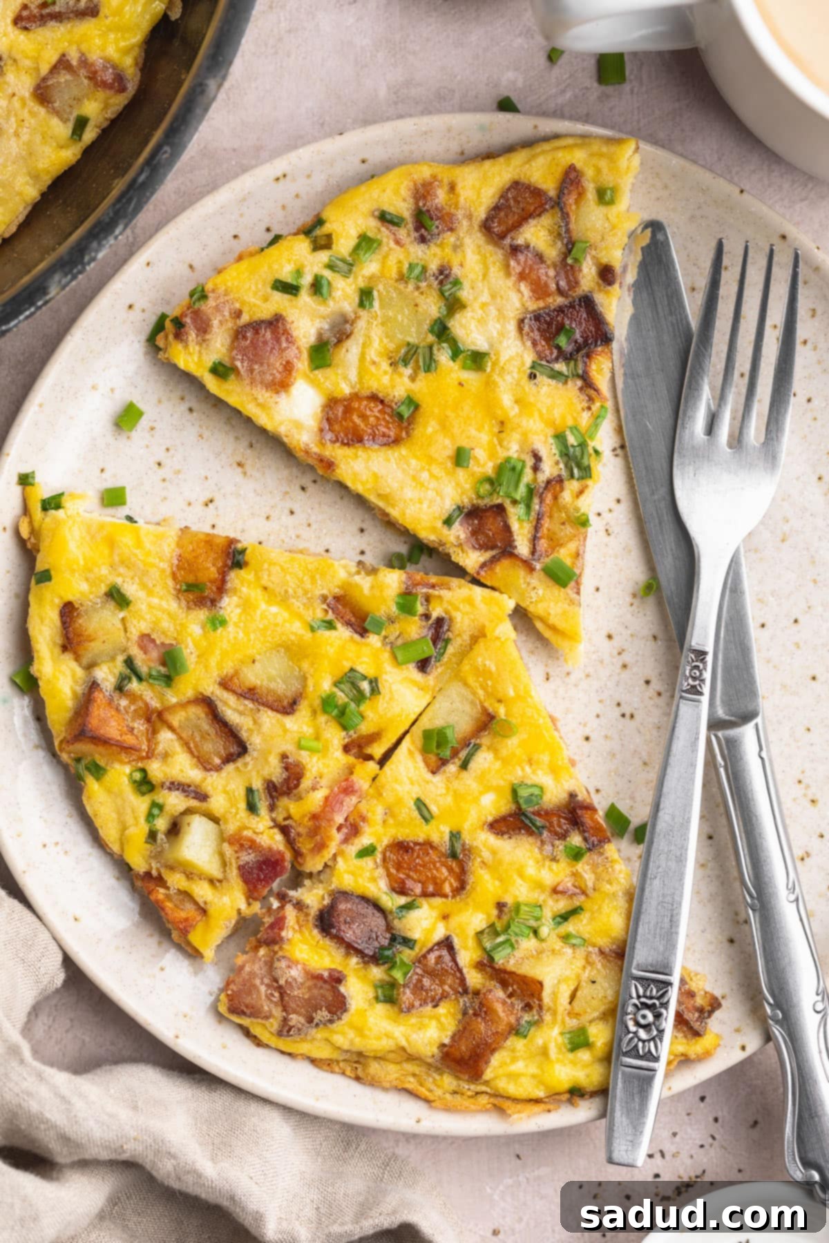 A country omelette, elegantly sliced into triangular wedges, served on a white plate with a fork and knife, garnished with fresh chives.