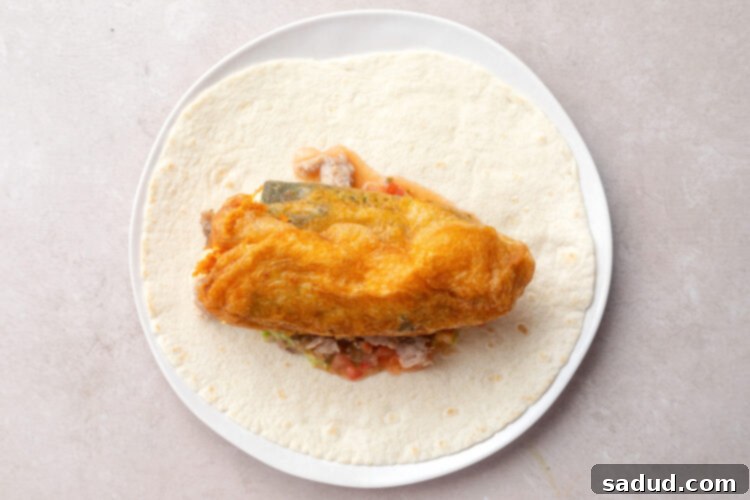 Unrolled chile relleno burrito with a chile rellano on top.
