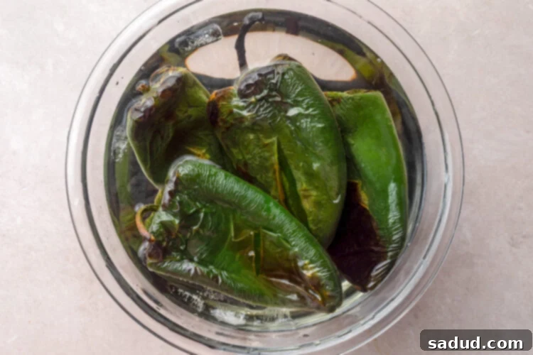 Charred and blistered poblano peppers in a bowl of cold water.
