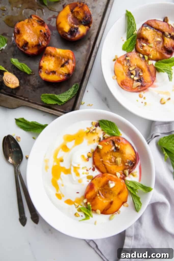 Artfully arranged grilled peaches drizzled with honey, served on two elegant white plates with a sprig of mint