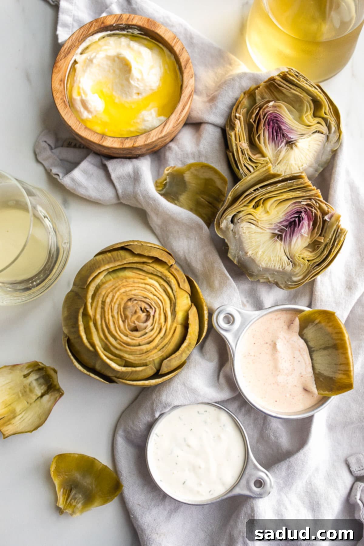 Boiled artichokes on a table with three different dipping sauces, ready to be enjoyed.
