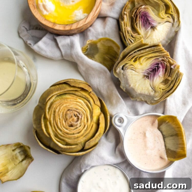 Boiled artichokes on a table with three different dipping sauces.