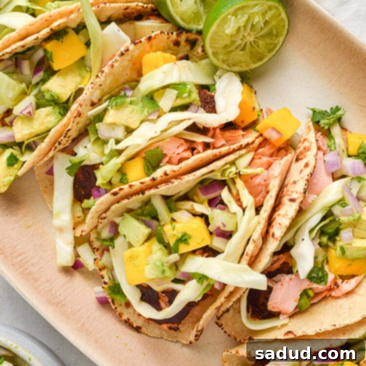 Four salmon tacos generously topped with vibrant slaw and sweet mango salsa, presented on an attractive oval platter, ready to be enjoyed.
