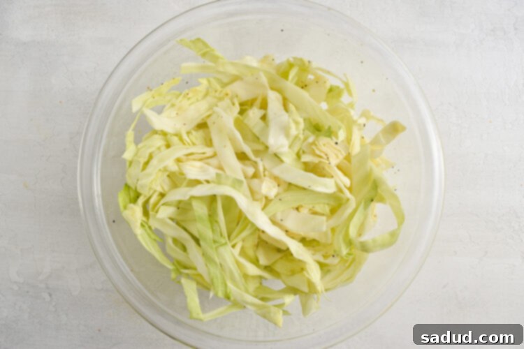 Simple homemade slaw with shredded cabbage in a medium glass mixing bowl, ready to be refrigerated for optimal flavor development.