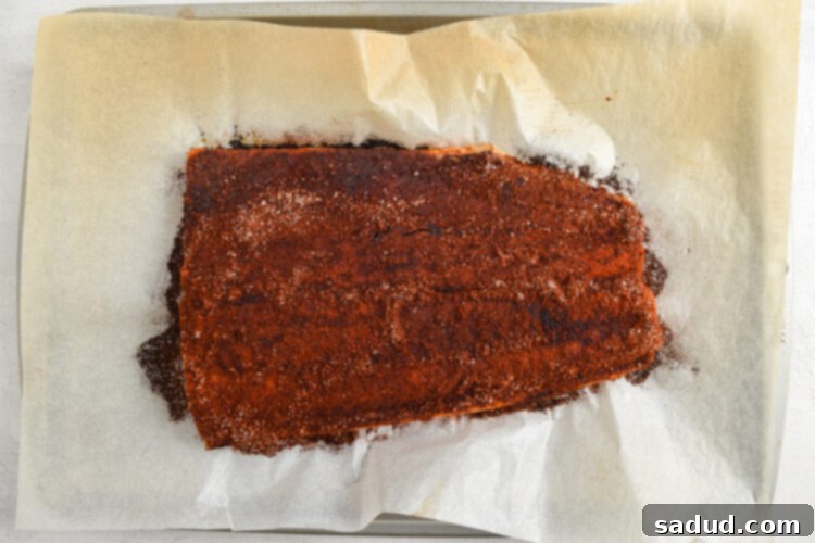 Seasoned salmon fillet resting on a baking sheet lined with parchment paper, perfectly prepped for baking.
