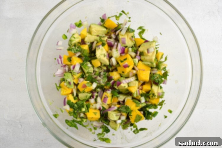 Beautifully prepared avocado mango salsa in a clear glass mixing bowl, showcasing vibrant colors and fresh ingredients.