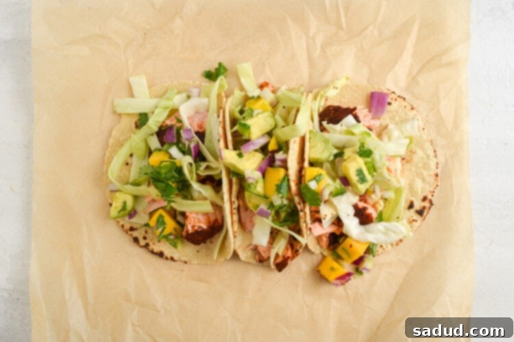 Assembled salmon tacos on a sheet of parchment paper, showcasing the flaky salmon, colorful slaw, and fresh mango salsa.