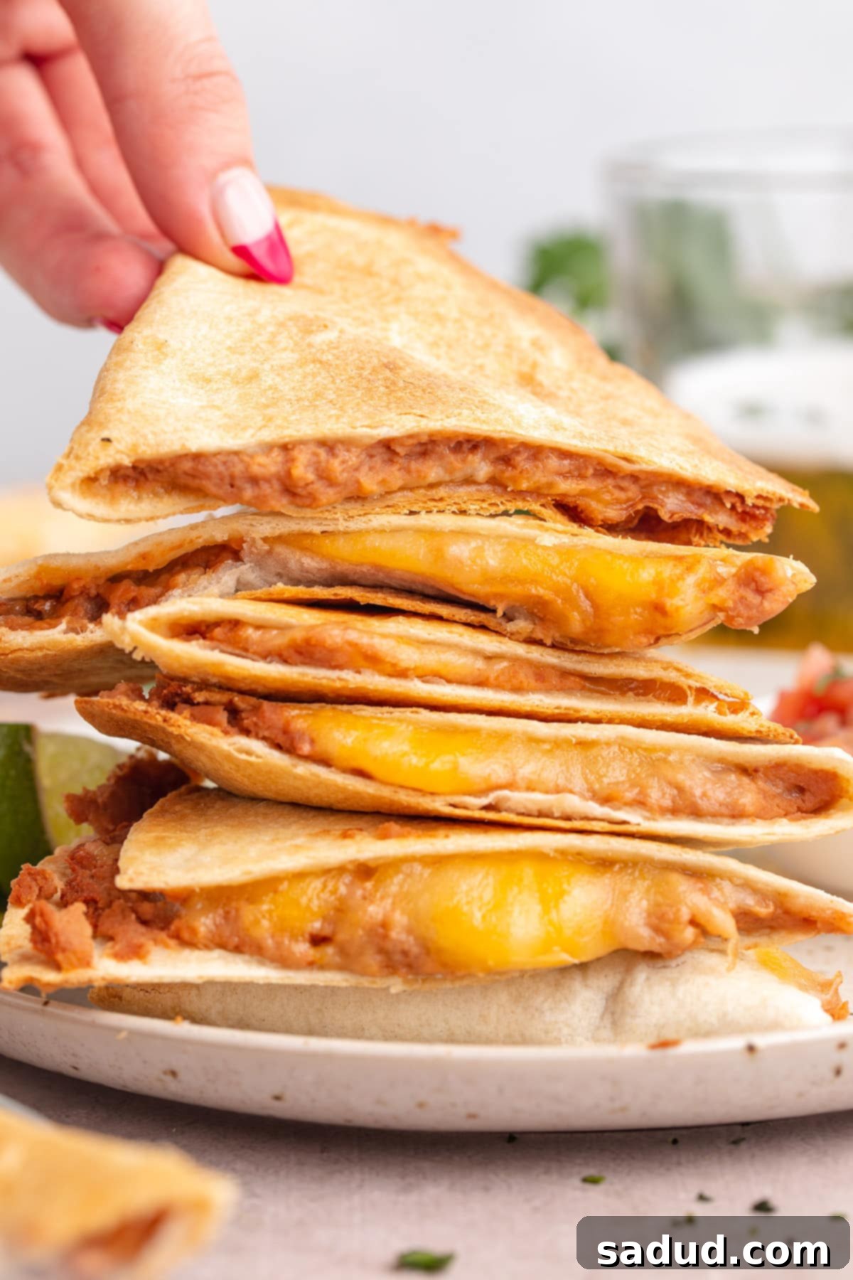 A white woman's hand picking up a triangular quesadilla slice from a stack of quesadilla slices.