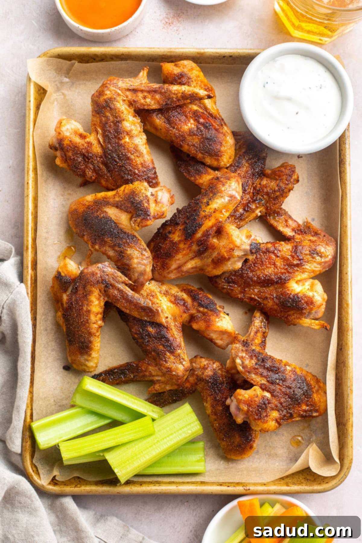 Whole chicken wings on a baking sheet lined with parchment paper next to a ramekin of ranch dressing.