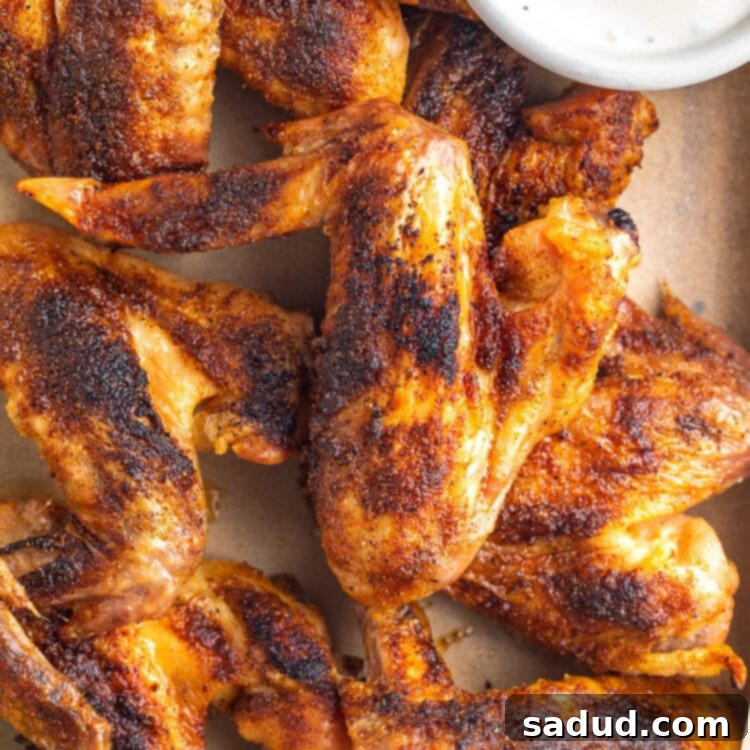 Whole chicken wings on a baking sheet lined with parchment paper next to a ramekin of ranch dressing.