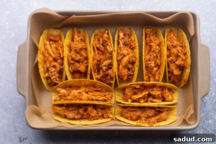 Crunchy taco shells arranged upright in a baking pan, filled with the savory shredded chicken mixture.