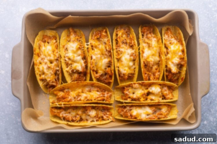 A baking pan filled with golden brown baked chicken tacos topped with melted cheese, fresh from the oven.