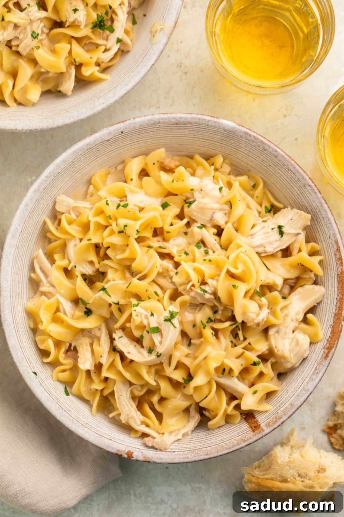 Overhead view of two bowls of Instant Pot chicken and noodles on a white table top with glasses of white wine.