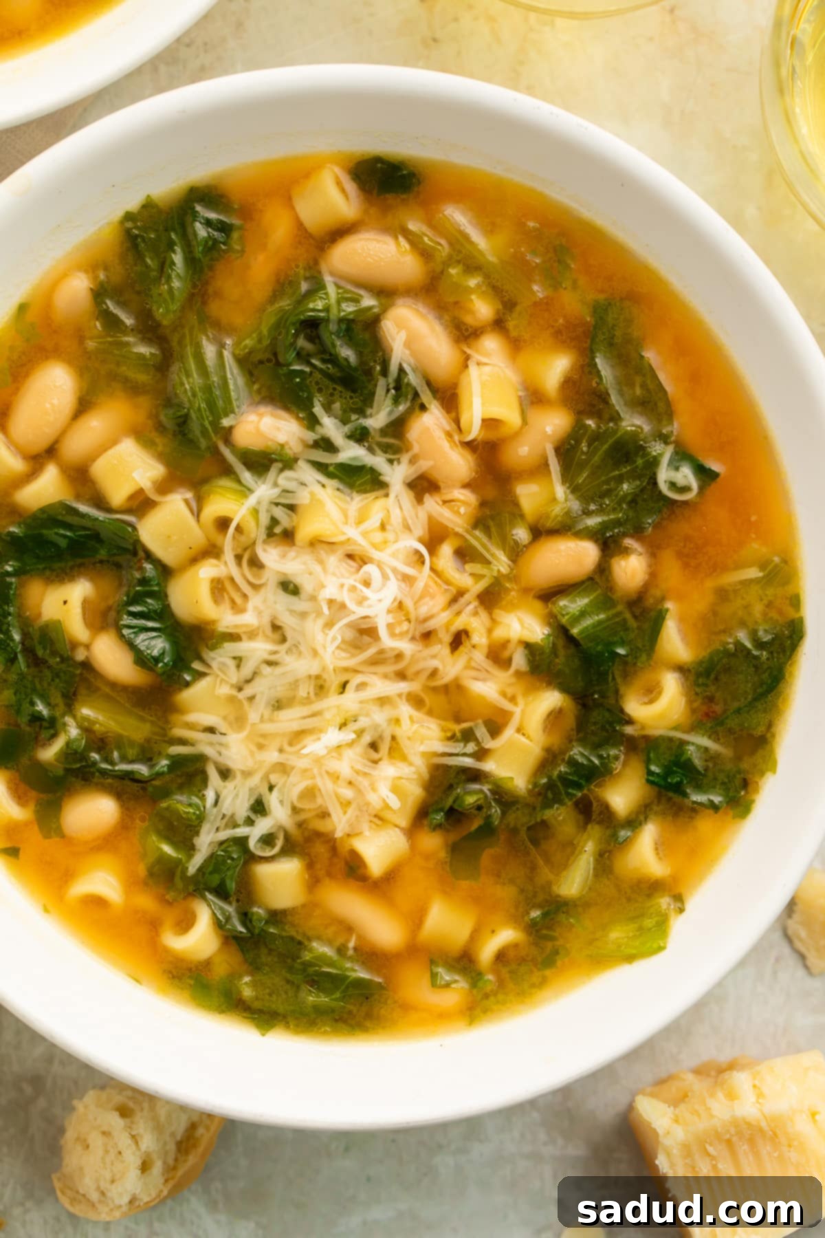 Close-up, overhead view of a white soup bowl filled with escarole soup, made up of short tube noodles, beans, and greens.