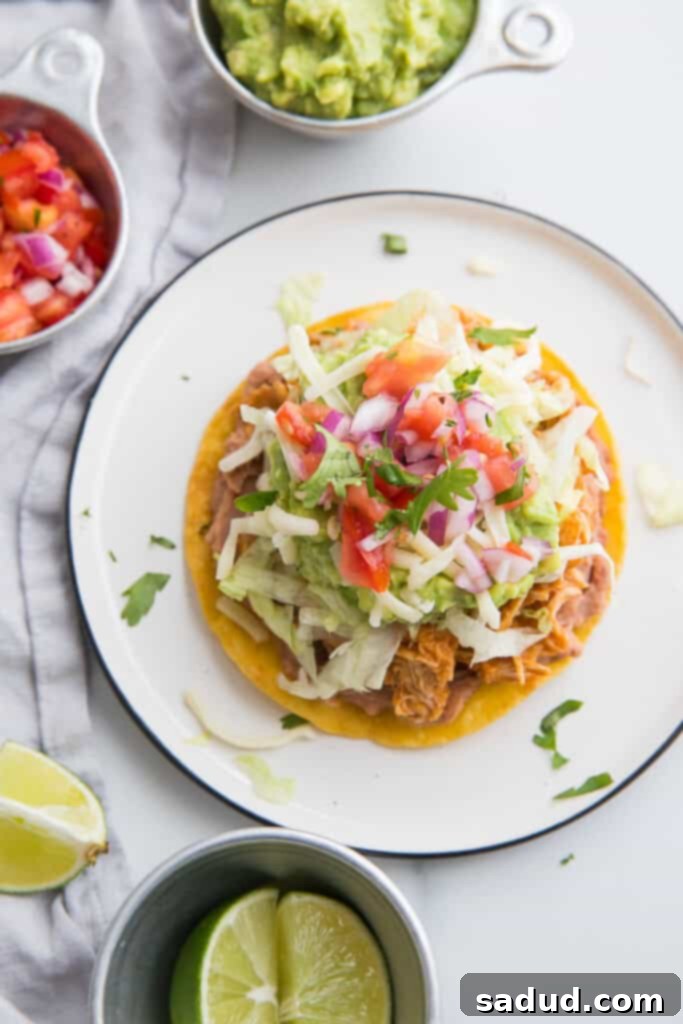 Chicken tostadas served on a white plate with small bowls of toppings around it
