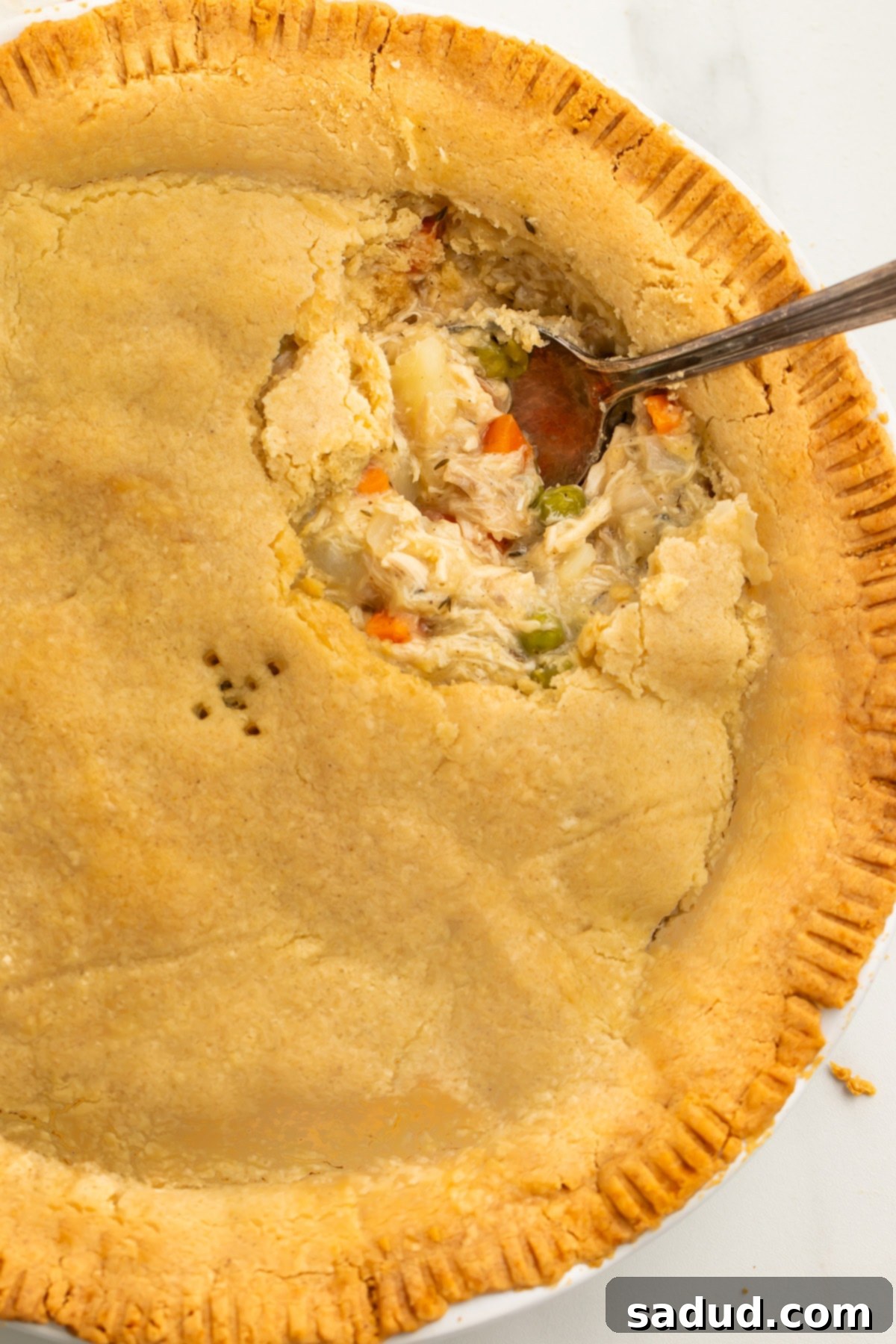 Overhead view of gluten free chicken pot pie in a pie plate, with a large scoop of chicken pot pie missing, showcasing the delicious golden crust.