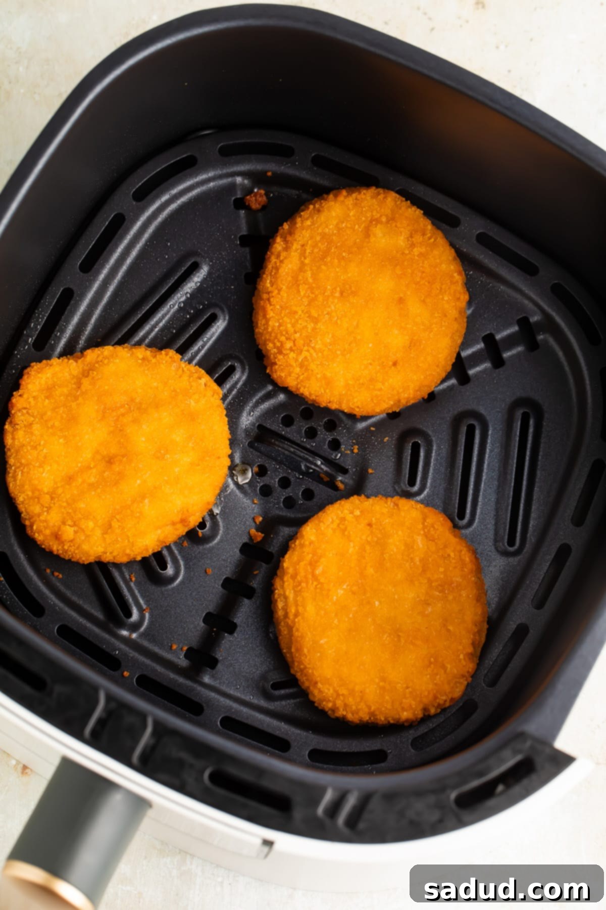 Three golden-brown chicken patties arranged neatly inside an air fryer basket, ready to be served.
