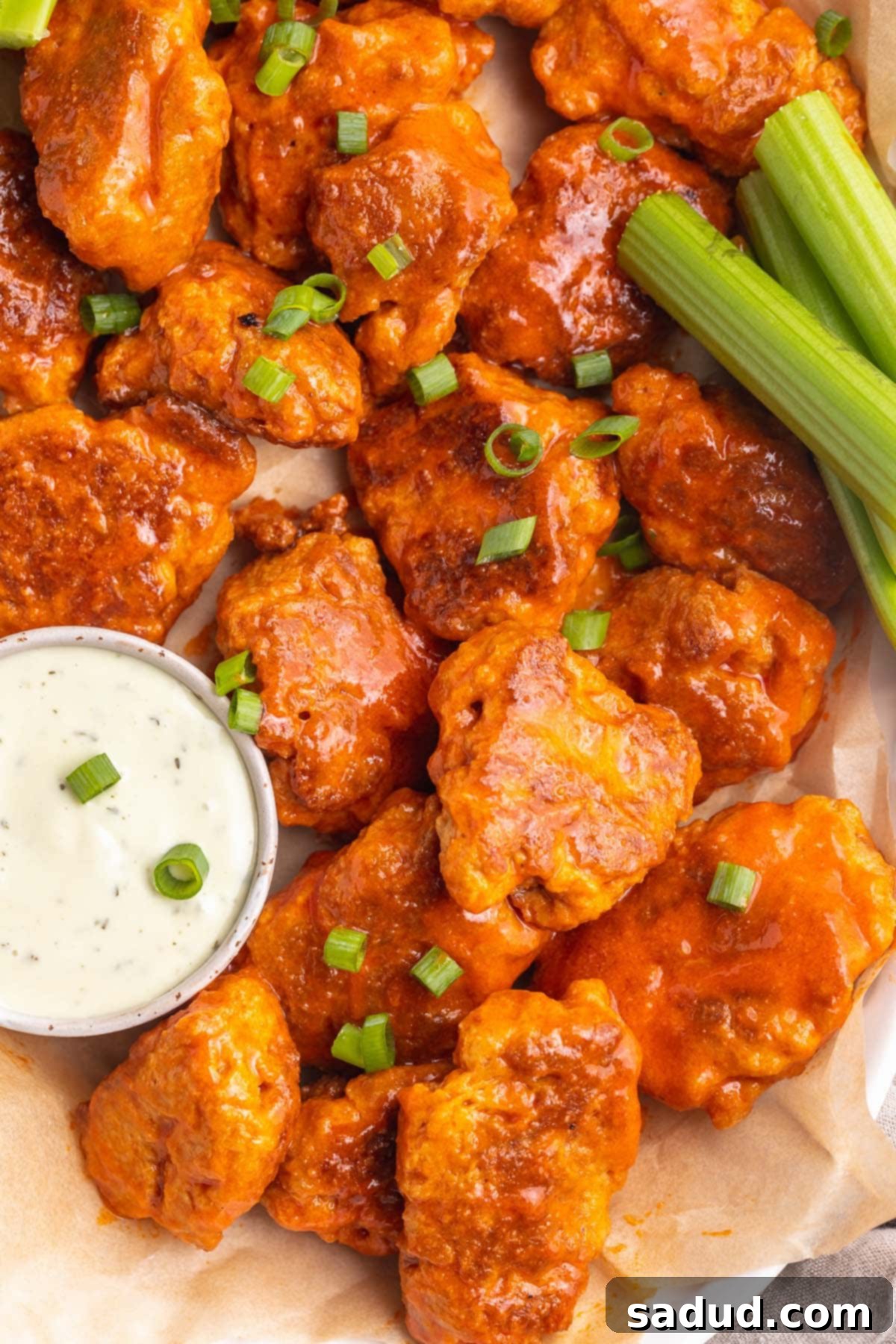 Buffalo sauced seitan wings on a platter with ranch dressing and celery sticks, ready to be served as a plant-based appetizer.